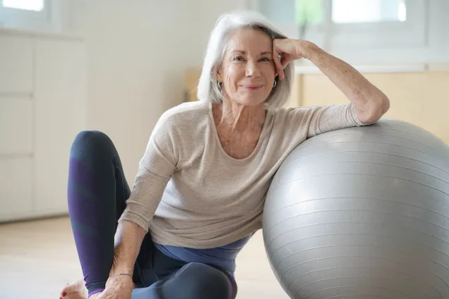 grey-haired woman sitting with exercise ball